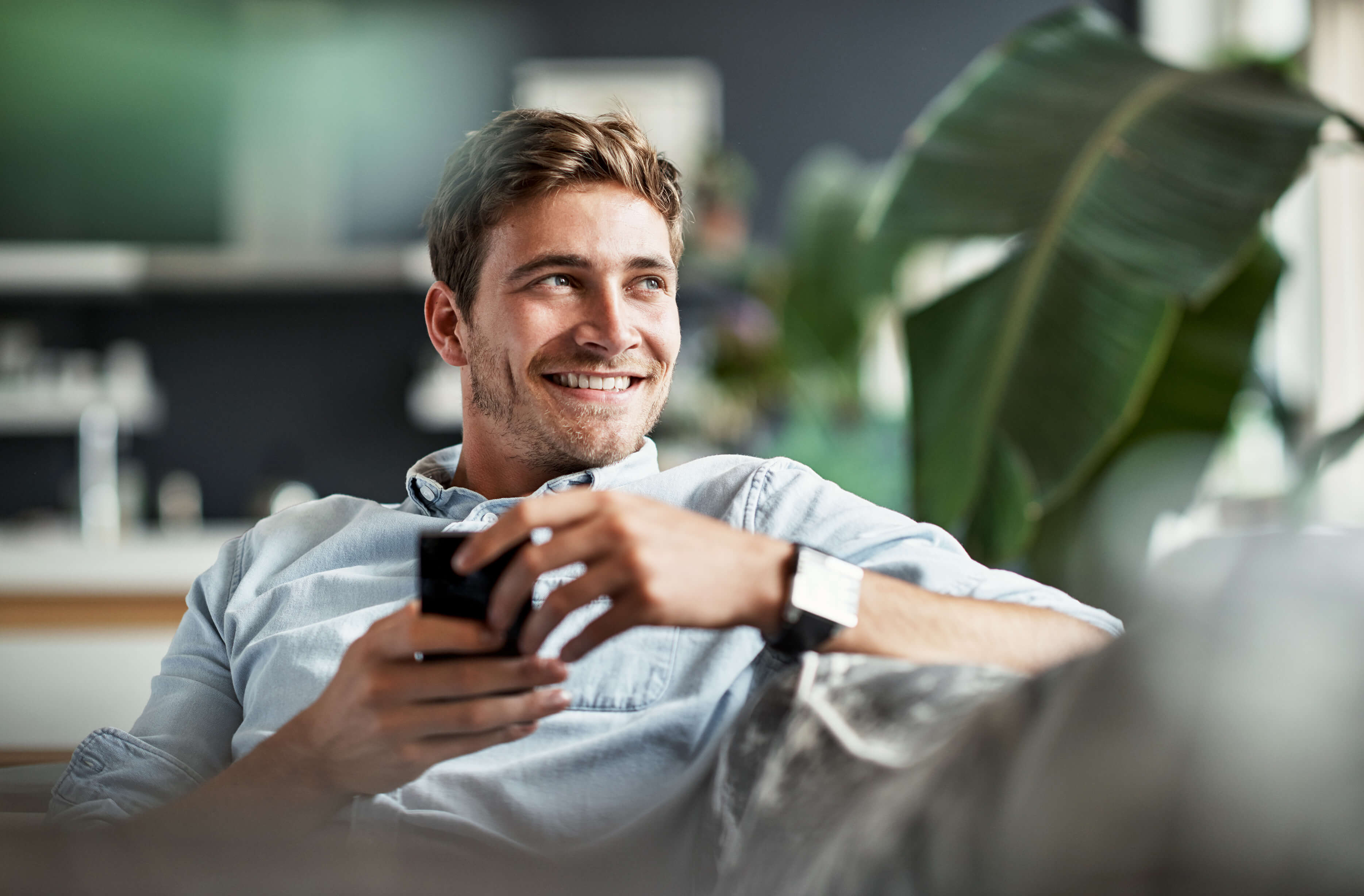 Man on sofa holding his phone and smiling